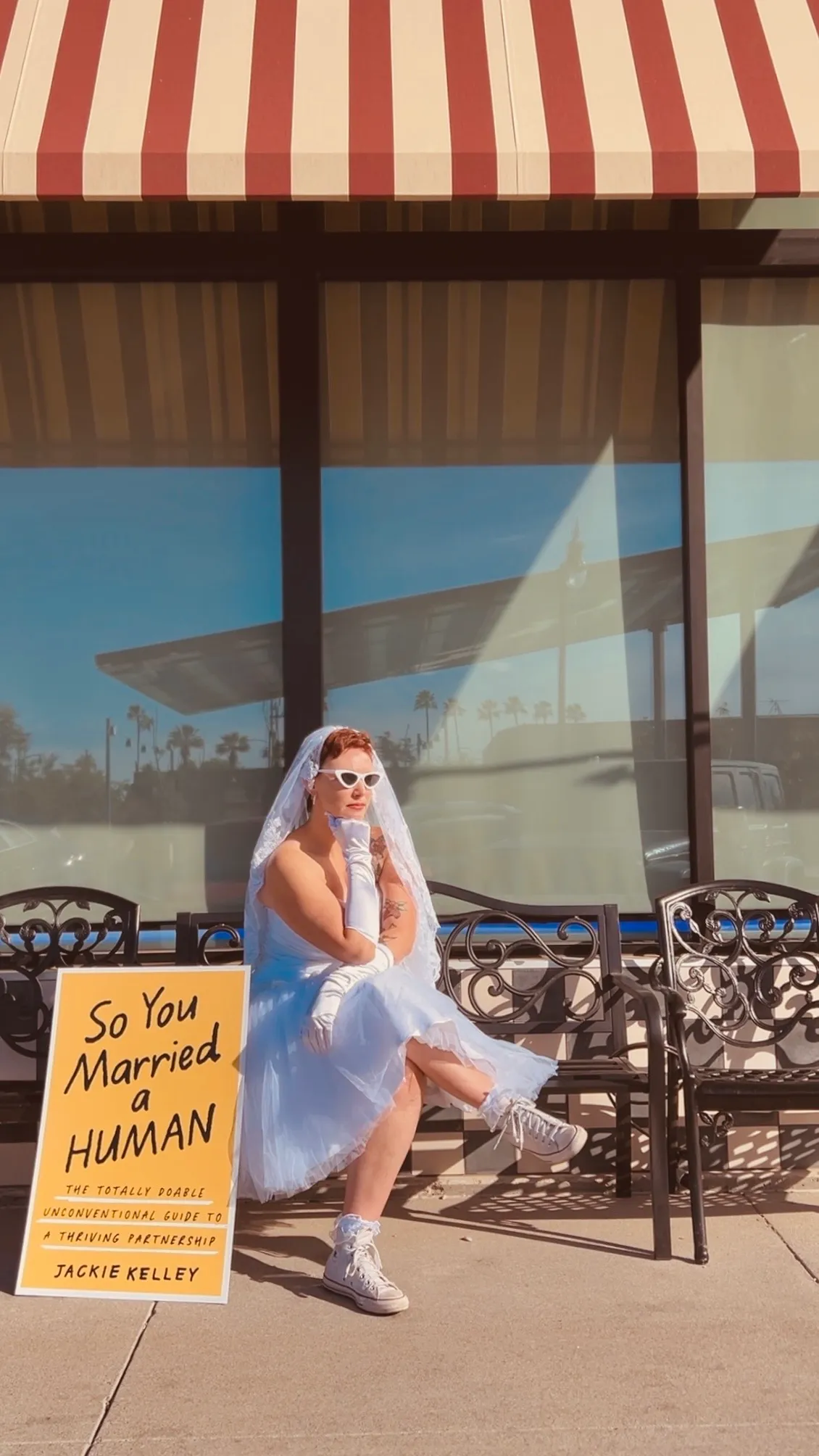 Jackie Kelley sitting on a bench under a striped awning, the four-foot printed cover propped beside her.