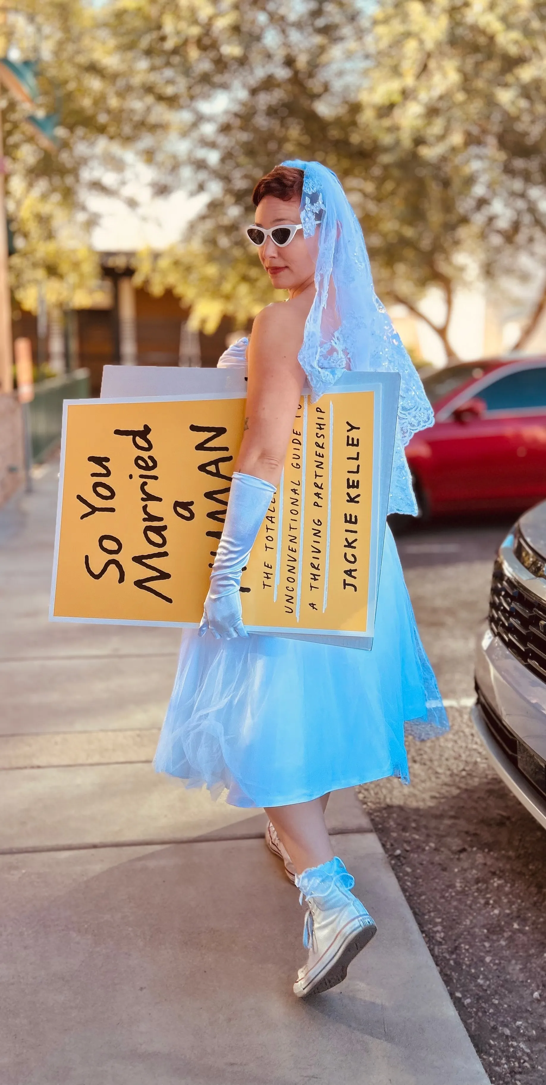 Jackie Kelley carrying the four-foot printed cover down a sidewalk in a blue tulle dress and gold high-tops.
